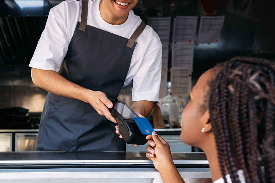 Image of a food truck owner holding a POS terminal while a customer pays by a contactless card