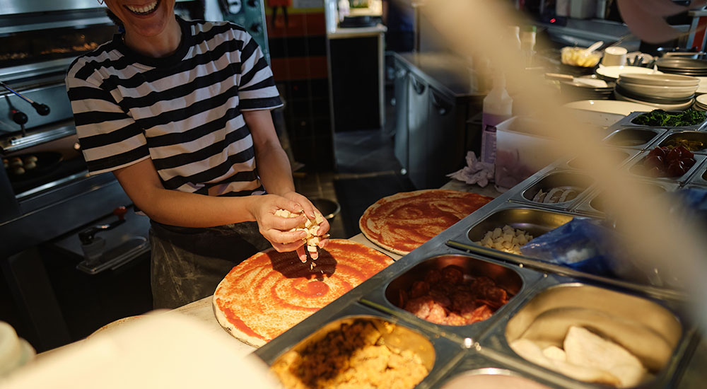 Image of woman working in the kitchen of a pizzeria.